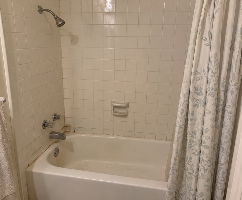 The same bathroom before work started: a dated tub and shower with small white tile and stained grout