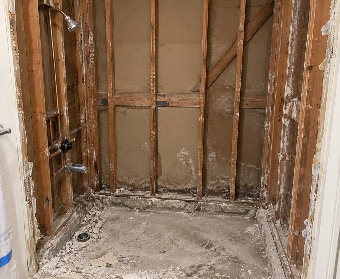 The same bathroom stripped to the studs, showing old plumbing and damaged framing before waterproofing